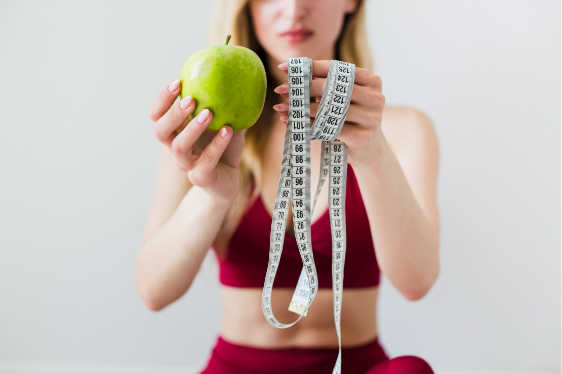 A woman holding an apple and a measuring tape, symbolizing macro-based fat loss.