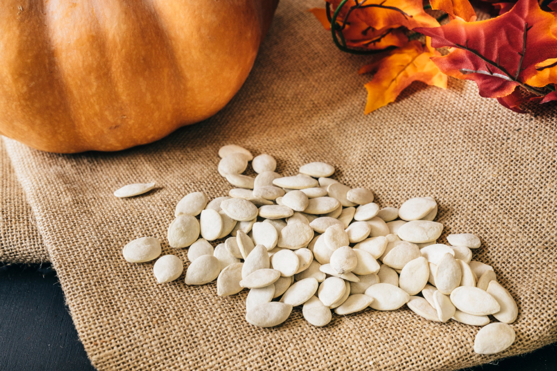 Pumpkin seeds scattered on a wooden surface with a small bowl, symbolizing natural energy.