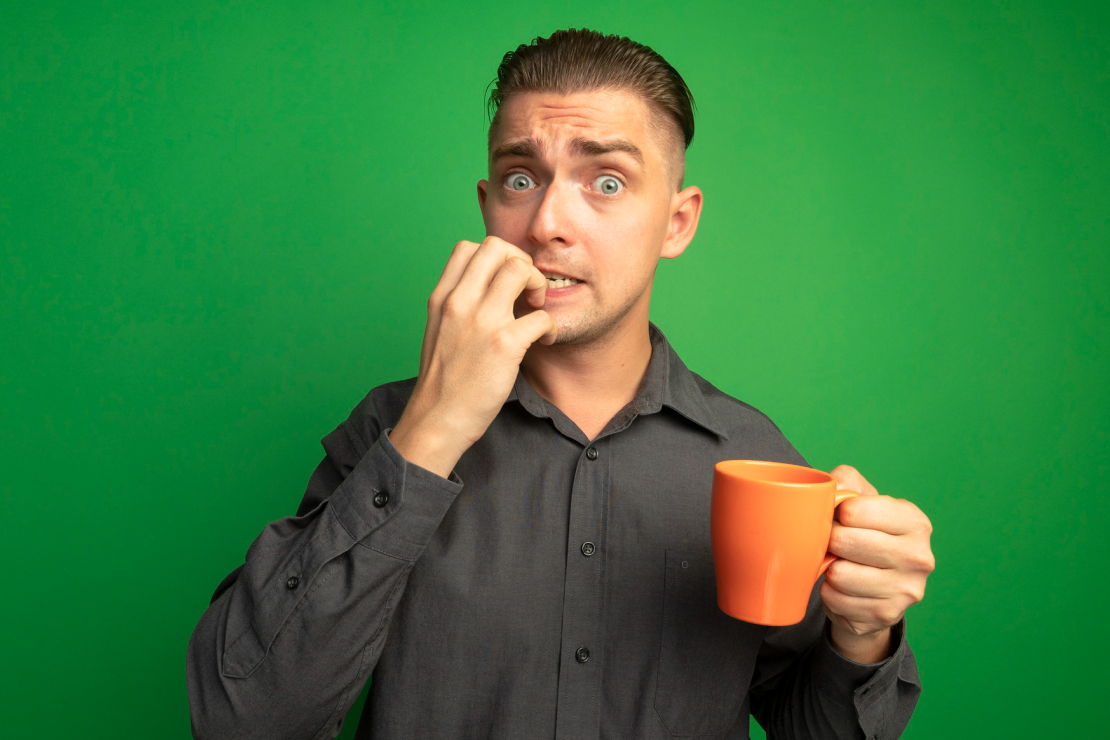 A man holding a coffee mug with a worried or anxious expression against a green screen, symbolizing the anxiety and myths surrounding coffee consumption.