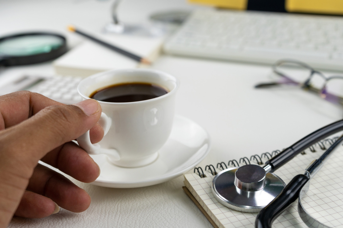 A cup of coffee on a desk next to a stethoscope and medical charts, symbolizing the scientific and health-related aspects of caffeine and metabolism.