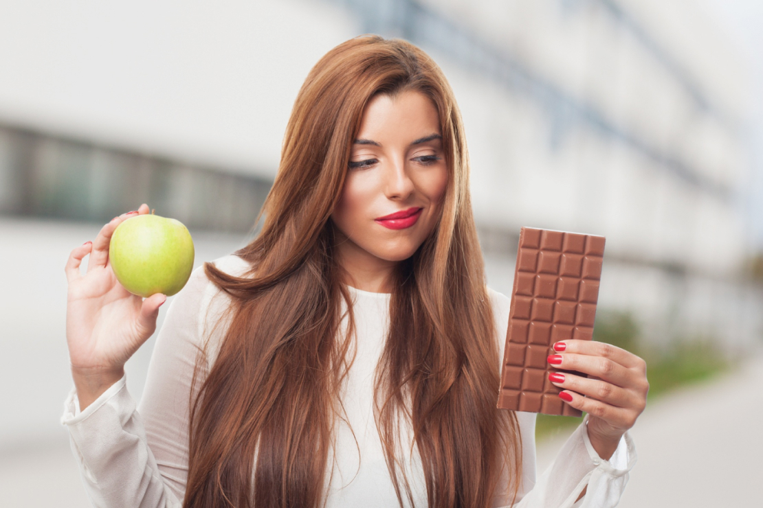 Woman holding a green apple and chocolate bar, representing healthy choices