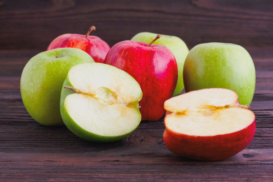 Assortment of red and green apples, some sliced, on a wooden surface, symbolizing healthy snacking.