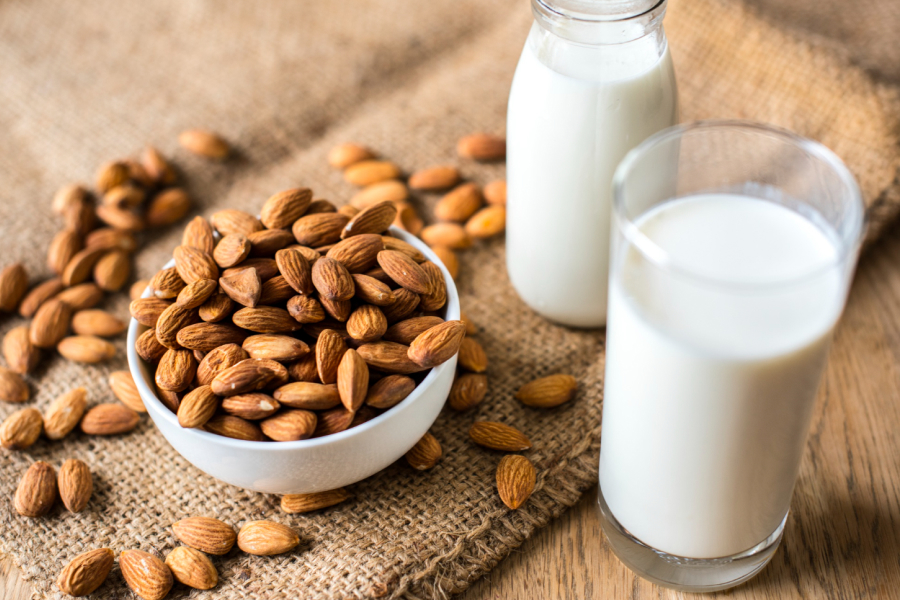 A bowl of almonds next to a glass and bottle of almond milk.