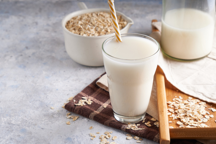 A glass of oat milk with oats scattered around, emphasizing its grain origin.